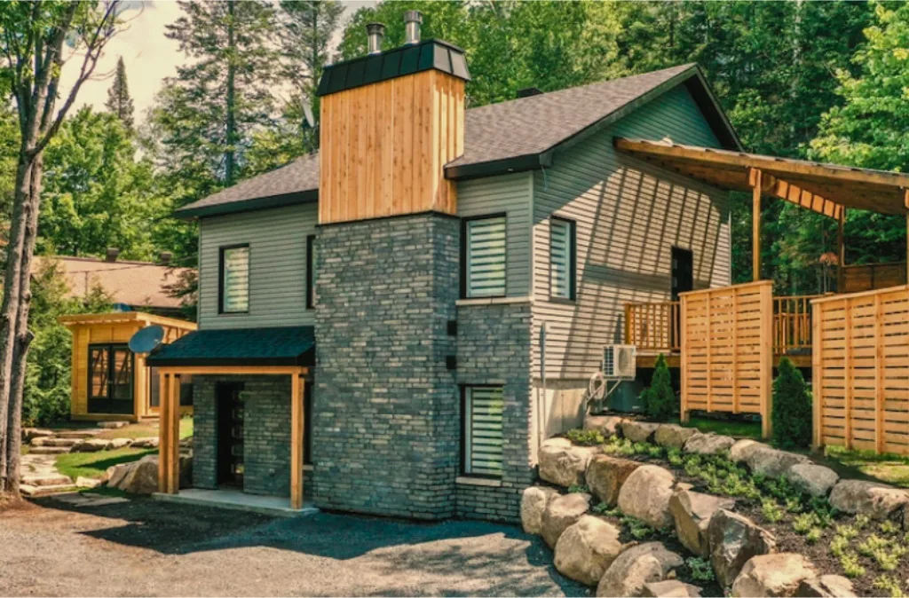 Rendu 3D d'une maison verte avec cheminée en bois et pergola, en forêt